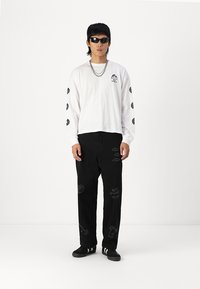 Long-sleeve white cotton shirt with graphic prints, paired with black cotton pants featuring various artistic designs. Black sneakers complete the look.
