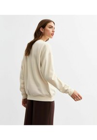 Ljuskrämfärgad sweatshirt med avslappnad passform, ribbad ärm- och nederkant. Mjuk, slät textur; insydda ärmar; minimalistisk design.