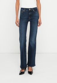 Jeans din denim albastru închis, cu croial�ă dreaptă, estompare subtilă și buzunare frontale. Purtate cu pantofi negri cu toc înalt.