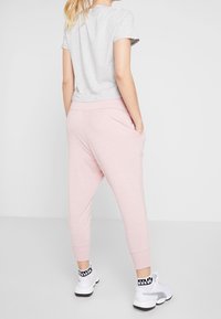 Grijs T-shirt met korte mouwen gecombineerd met roze joggers met zakken. Witte sneakers met zwart-wit geblokte sokken.