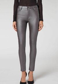 Jeans skinny grigio metallico con texture liscia, dotati di tasche anteriori, passanti per cintura e chiusura con bottone. Indossati con tacchi alti neri.