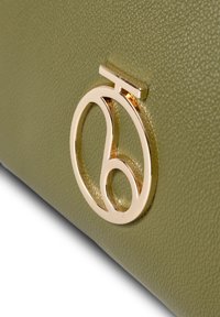 Olijfgroene leren tas met textuur en een opvallend gouden cirkelvormig logo. Het oppervlak heeft een gestructureerde afwerking voor extra textuur.