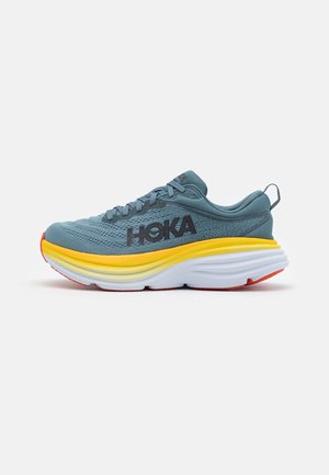 Scarpa da corsa blu con logo HOKA nero, suola spessa gialla e bianca, e suola rossa, mostrata di lato su sfondo bianco.