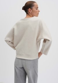 Maglione beige chiaro a pullover con una vestibilità ampia, maniche larghe e scollatura rotonda, abbinato a jeans grigi chiari a sigaretta. Texture liscia.