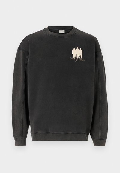 Svart hettegenser laget av mykt materiale, med rund hals og senkede skuldre. Forsideprint av tre figurer med tekst under.