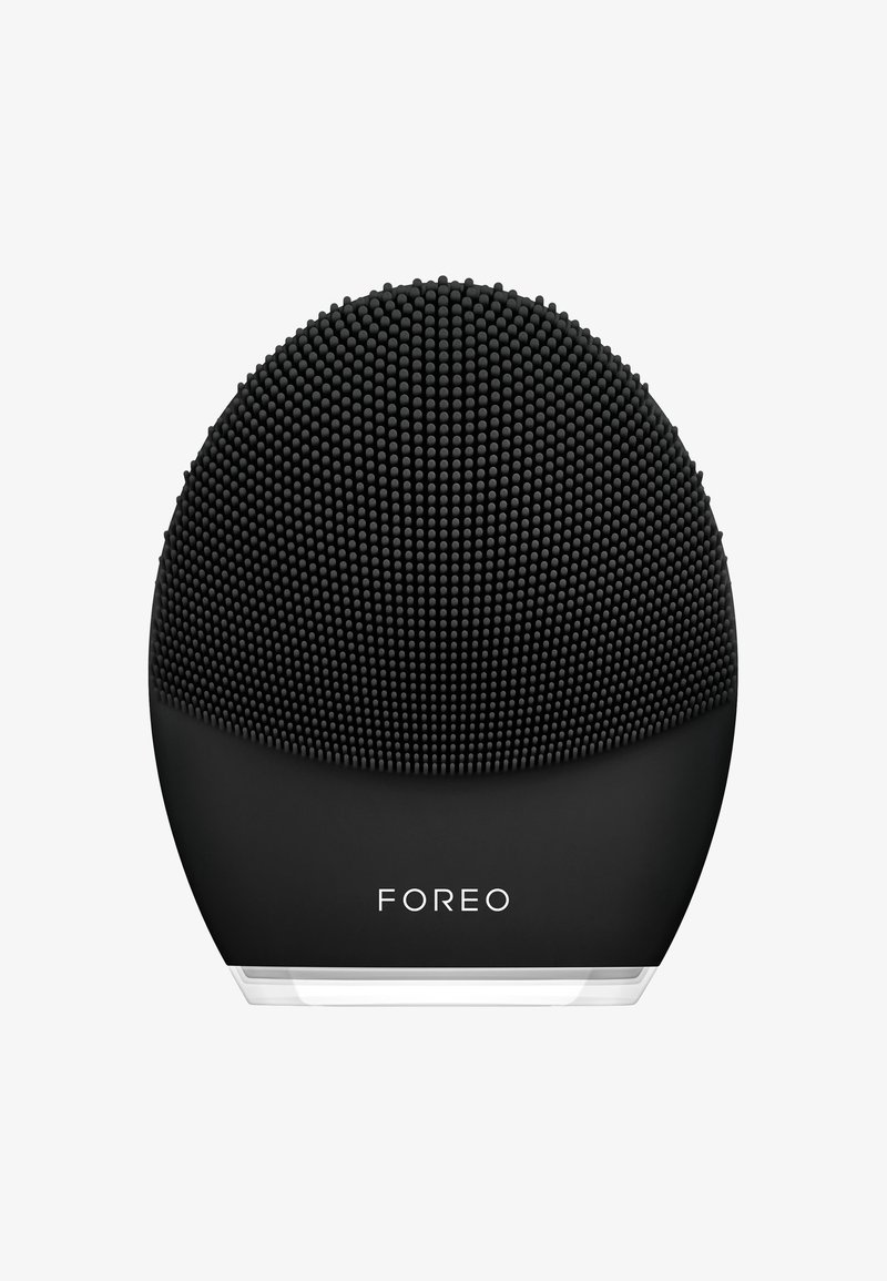 Dispositif de nettoyage facial en silicone noir avec une surface texturée et ponctuée, une forme arrondie et une base transparente portant le nom de la marque "FOREO".
