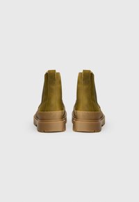 Zelené kožené členkové topánky s elegantným dizajnom, majúce hladký povrch, kontrastnú hnedú gumovú podrážku a zadné pútka na obúvanie.