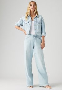 Lys blå denimjakke med rullede ermer, kombinert med lys blå vide jeans med strikk i livet. Hvit tettsittende genser under.