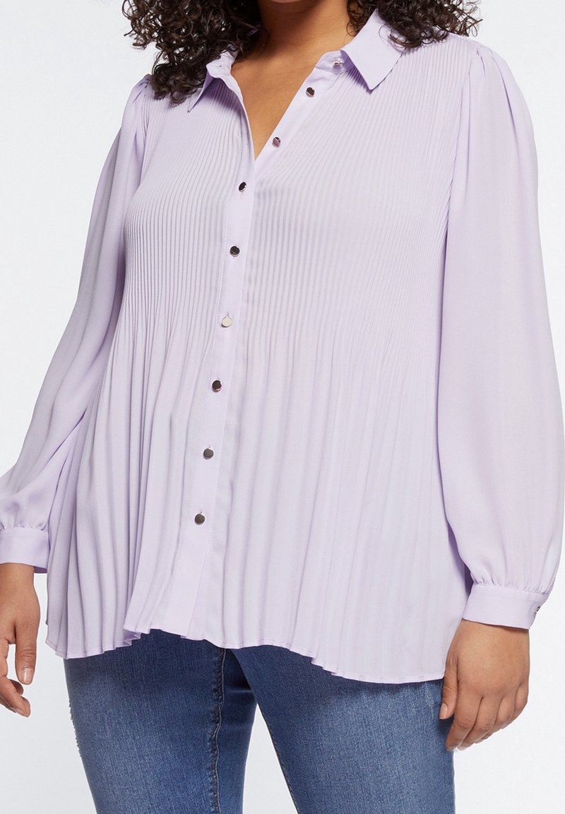 Lila plisserad blus med knäppning fram, långa ärmar och rund nederkant. Har silverknappar som accent och är tillverkad av mjukt, lätt tyg.