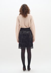 Világos bézs, bolyhos pulóver, amely oversized stílusú, fekete rojtos szoknyával párosítva. Fekete harisnyák és pántos cipők egészítik ki az öltözéket.