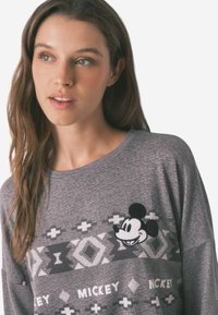 Gray sweatshirt featuring a textured pattern with geometric shapes and a Mickey Mouse applique. Crew neck and loose fit design.