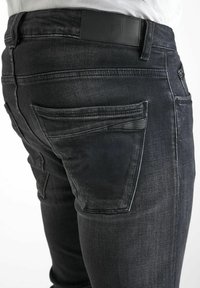 Jean en denim délavé foncé à coupe slim. Présente une étiquette de taille en cuir noir et des poches arrière classiques avec des détails de couture discrets.