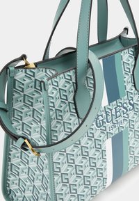 Miętowa zielona torebka z geometrycznym wzorem, podwójnymi uchwytami i regulowanym paskiem. Posiada logo oraz niebiesko-białe paski jako akcenty.