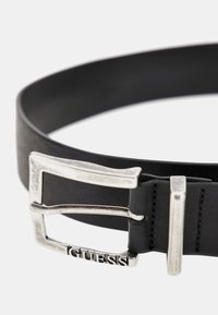 Cintura in pelle nera con una fibbia rettangolare argentata con la scritta "GUESS" incisa. Texture liscia, design minimalista e forma tradizionale.