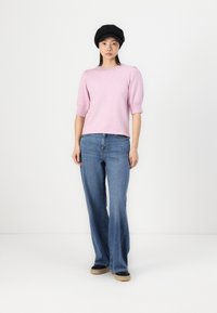 Light pink short-sleeve sweater with puffed shoulders, paired with wide-leg blue denim jeans and black flat cap, set against a white background.