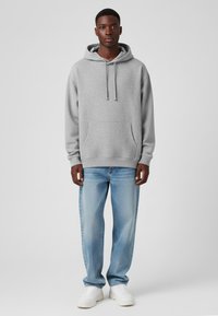 Felpa grigia con tasca a marsupio, stringhe regolabili, polsini a costine, abbinata a jeans straight leg blu chiaro e sneakers bianche.