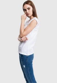 Camiseta blanca de algodón con panel de encaje en los hombros, combinada con jeans ajustados rasgados azules. La tela es suave y ceñida.