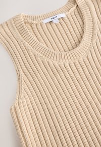 Krémový bezrukávový sveter s rebrovanou textúrou a okrúhlym výstrihom. Na zadnej strane je štítok s nápisom "NEXT".