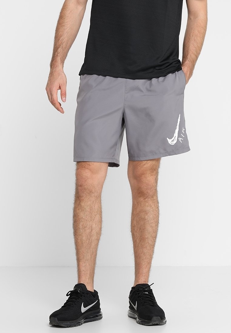 Homme portant un short Nike Air gris, un T-shirt noir et des baskets Nike noires, debout devant un fond clair uni.