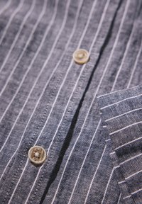 Blauw gestreept stoffen overhemd met een gestructureerde weving, met witte verticale strepen, kunststof knopen en een zak aan de linkerkant.