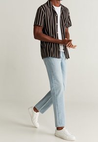 Camisa de rayas blancas y negras de manga corta, llevada sobre una camiseta blanca, combinada con jeans de mezclilla azul claro y zapatillas blancas. Ajuste casual.