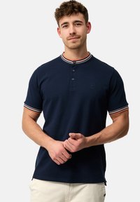 Marineblå polo T-shirt med korte ærmer, tre knapper ved kraven og stribede ribbede detaljer i rød, hvid og blå på halsudskæringen og ærmerne.