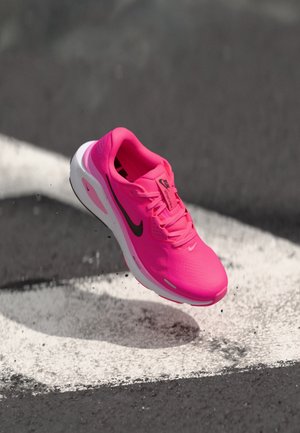 Bright pink Nike running shoe mid-air above a black and white painted road surface.