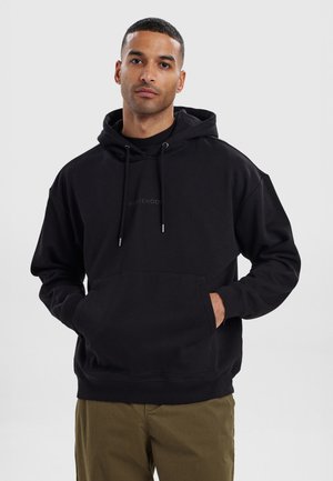 Black hooded sweatshirt with drawstrings and a front pocket, featuring a subtle logo in the center. Soft, brushed fabric texture.