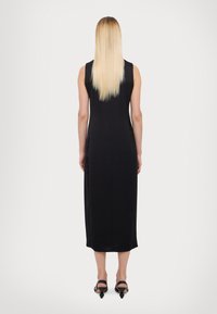 Rochie neagră fără mâneci, până la genunchi, design mulat, material neted, fermoar ascuns la spate, purtată cu sandale negre plate.
