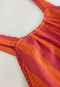 Sundress med orange och rosa vertikala ränder, med justerbara axelband, veckad detalj vid halsringningen och ett lätt, texturerat tyg.