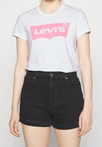 White cotton t-shirt with a pink Levi's logo, paired with black denim shorts featuring rolled hems and front pockets.