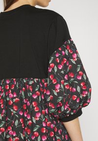 Czarna bluzka z krótkimi, bufiastymi rękawami, z kontrastowym materiałem ozdobionym nadrukiem wiśni na ciemnym tle.