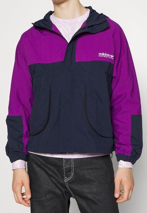Person wearing a two-tone purple and navy Adidas Adventure jacket with a front zipper and elastic cuffs.