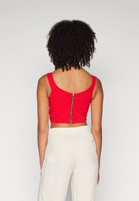 Top corto rosso con spalline larghe e una zip argentata sul retro, abbinato a pantaloni chiari e larghi.