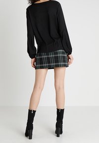 Top nero a maniche lunghe abbinato a una mini gonna a scacchi verde e bianca, completato da stivali neri con tacco alto alla caviglia con cerniere.