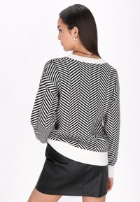 Pulover herringbone alb și negru cu tiv și manșete albe cu nervuri, având o croială lejeră și un detaliu de tricotaj texturat.