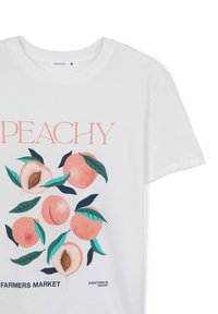 T-shirt bianco in cotone con un design grafico di pesche rosa e foglie verdi. Il testo recita "PEACHY" e "FARMERS MARKET."