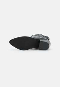 Czarny skórzany botek za kostkę leżący na boku, pokazujący gładką podeszwę i niski blokowy obcas na białym tle.