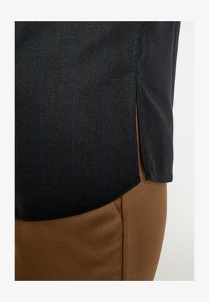 Zwart herringbone stoffen overhemd met blauwe strepen, voorzien van een zijsplit. Gecombineerd met gladde bruine stoffen broek, met strakke lijnen en snitten.