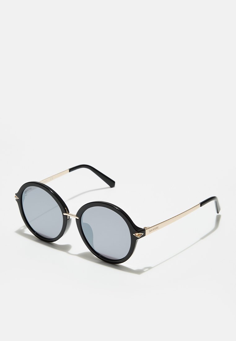 Ronde zonnebrillen met zwarte kunststof monturen, grijze lenzen en gouden metalen accenten. Slanke pootjes en een lichte vleugeldetail aan de voorkant.