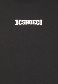 Czarny bawełniany t-shirt z białym haftowanym napisem "DCSHOECO" w wyrazistym kroju na środku klatki piersiowej. Gładka tekstura i klasyczny krój.
