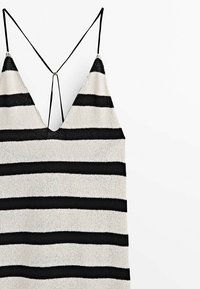 Débardeur en tricot à rayures noires et blanches alternées, avec un profond décolleté en V et de fines bretelles noires dans le dos. Texture douce.