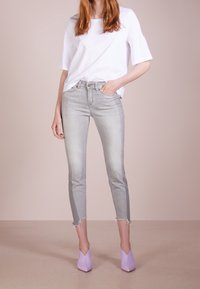 Jeans skinny grigio chiaro in cotone con orli sfrangiati, abbinati a una t-shirt bianca a maniche corte e décolleté viola lavanda con punta.