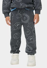 Dunkelgraue Jogginghose mit weißen cartoonhaften Designs, elastischem Bund mit Kordelzug, Bündchen an den Knöcheln, kombiniert mit weißen Sneakern.
