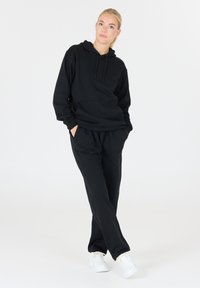 Zwarte hoodie met trekkoord en een voorzak, gecombineerd met bijpassende joggingsbroeken. De stof lijkt zacht en het ontwerp is eenvoudig en casual.