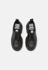 Black sneakers made of leather with a thick rubber sole. Features laces, a pull tab, and bold branding on the insoles. Stylish, modern design.