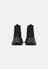 Black knit ankle sneakers with elastic panels, rubber soles, and subtle branding on the heel. Features a streamlined design and textured accents.