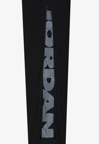 Črne trenirke z bleščečim sivo "JORDAN" logotipom ob strani. Imajo zadrgo ob bočni šiv. Narejene so iz gladkega materiala.
