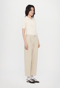 Cream knit polo shirt with button placket, paired with light beige wide-leg trousers and black shoes with accents. Plain white socks.