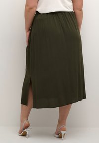 Olive green, knee-length skirt made from lightweight fabric; features a side slit and waistband; paired with silver heeled sandals.